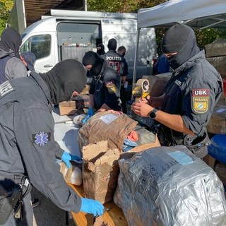 Vermummte Personen des LKA untersuchen Gegegenstände in großen Kartons, die bei einer Razzia in Reutlingen am 09.10.24 beschlagnahmt wurden.