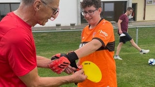 Ein Trainer des SV Vollmaringen hilft einer Spielerin dabei, die Handschuhe anzuziehen. Der Verein engagiert sich für Inklusion.