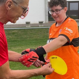 Ein Trainer des SV Vollmaringen hilft einer Spielerin dabei, die Handschuhe anzuziehen. Der Verein engagiert sich für Inklusion.