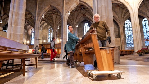 Eine Helferin und ein Helfer rollen die schweren Kirchenbänke aus der Tübinger Stiftskirche.