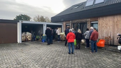 Menschen stehen mit Behältnissen vor der Garage von Josef Hugger, indem Kraut an einer Maschine geschnitten wird.