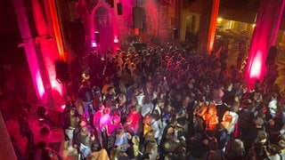 Viele Menschen tanzen ausgelassen bei der Clubnacht in der Stiftskirche Tübingen, die bei der Aktion Leer_raum zur bunt beleuchteten Party-Location wurde.