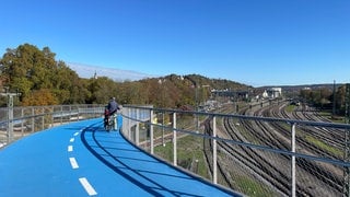 Ein älterer Herr und ein Junge stehen mit ihren Rädern auf der neuen Radbrücke West in Tübingen. Sie blicken in Richtung Schloss und Schlossberg. Zur anderen Seite liegt der Hauptbahnhof, den man ebenfalls gut beobachten kann.