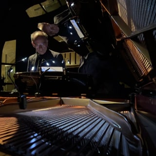 Andreas Grau von der Hochschule für Kirchenmusik steht an einem Flügel in der Tübinger Stiftskirche. Er hatte die Idee, das Musikstück "Vexations" aufzuführen.