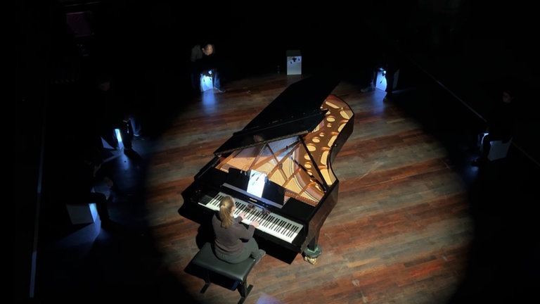 In der Stiftskirche Tübingen sitzt eine Pianistin am Flügel, die Kirche ist dunkel, nur die Fläche um den Flügel ist erleuchtet.