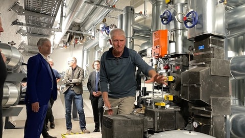 Boris Palmer sieht sich mit mehreren Leuten eine große Heizungsanlage an - sie ist im Schloss Hohentübingen frisch angebracht und an das Fernwärmenetz der Stadtwerke angeschlossen.