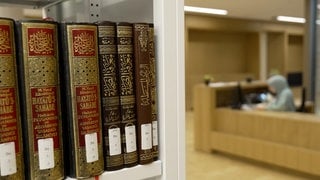 Bibliothek des Zentrums für islamische Theologie. Eine studentische Hilfskraft sitzt am Computer, im Vordergrund stehen islamische Lehrbücher.