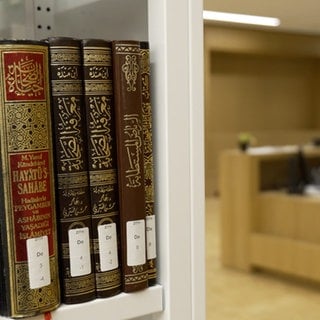 Bibliothek des Zentrums für islamische Theologie. Eine studentische Hilfskraft sitzt am Computer, im Vordergrund stehen islamische Lehrbücher.