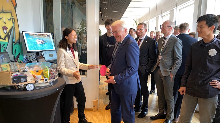 Beim KI-Wettbewerb in Tübingen darf Bundespräsident Steinmeier die Projekte ausprobieren. Hier hält er einen Tischtennisball mit dem Schläger oben.