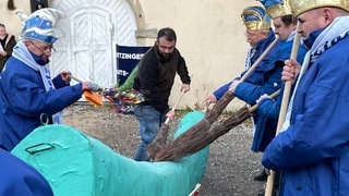 Vereinmitglieder der Betzinger Krautskräga stauben bei einer Veranstaltung einen großen Krautstrunk aus Ästen ab