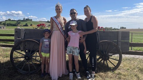 Familie Ferro steht mit Mrs World vor einem alten Heuwagen