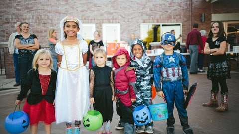 Kinder stehen in Halloweenkostümen in einem Raum und tragen bunte Kürbislaternen. An Halloween gibt es viele Events in der Region.