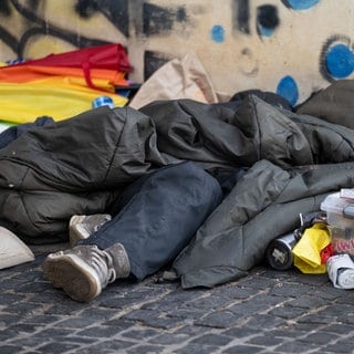 Eine Person liegt in der Innenstadt unter einem Schlafsack.