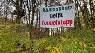 Ein Banner mit dem Schriftzug "Klimaschutz heißt Tunnelstopp" in einem Wald bei Tübingen. Aktivisten haben es aus Protest gegen den Schindhaubasistunnel angebracht. Der geplante Tunnel soll die B27 entlasten.