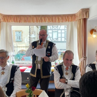 Mitglieder der Narrenzunft Vetter Guser in Sigmaringen sitzen an einem langen Tisch. Der  Zunftmeister Philippe Sutter hält eine reede zur Eröffnung der Fasnet.