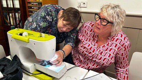 Eine Kursleiterin hilft einer Teilnehmerin bei der Bedienung der Nähmaschine. Aussortierte Kleidung kann in Reutlingen im Textil-Recycling-Café der Bruderhaus-Diakonie mitgebracht und zu Taschen und anderem umgenäht werden.