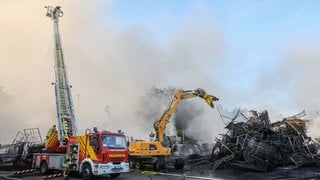 Einsatzkräfte der Feuerwehr stehen während des Großbrandes auf dem Gelände von Reifen Göggel und löschen das Feuer. 