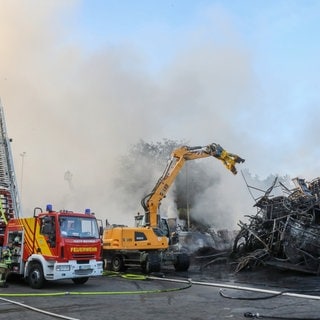 Einsatzkräfte der Feuerwehr stehen während des Großbrandes auf dem Gelände von Reifen Göggel und löschen das Feuer. 