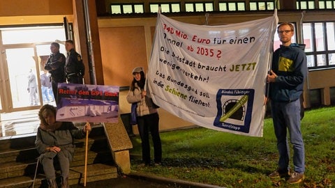 Aktivistinnen und Aktivisten haben vor der Halle der Infoveranstaltung mit Plakaten ihre Haltung gegen den Bau des Schindhaubasistunnels in Tübingen verdeutlicht