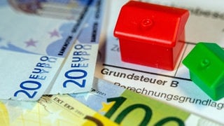 Geldscheine und symbolische Häuser: Für die Reform der Grundsteuer sind die Werte Immobilien neu festgelegt worden. In Reutlingen wird man für knapp die Hälfte der Grundstücke künftig mehr Grundsteuer zahlen müssen. 