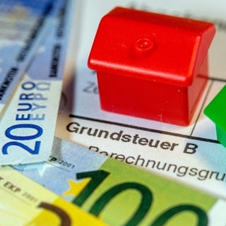 Geldscheine und symbolische Häuser: Für die Reform der Grundsteuer sind die Werte Immobilien neu festgelegt worden. In Reutlingen wird man für knapp die Hälfte der Grundstücke künftig mehr Grundsteuer zahlen müssen. 