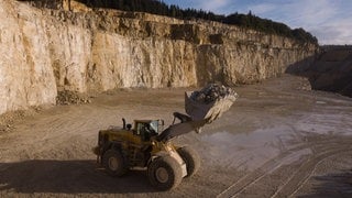 Ein Radlader steht im Steinbruch in Straßberg (Zollernalbkreis). Seine Schaufel ist voll mit Gestein. Künftig wird in dem Steinbruch wegen der Streichung von Arbeitsplätzen weniger gearbeitet.