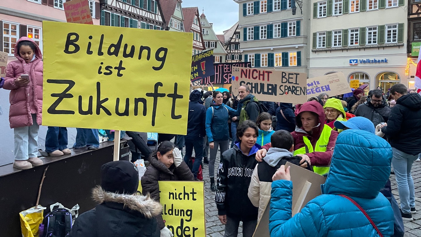 Schüler, Lehrer und Eltern halten bunte Protestplakate auf dem Tübinger Marktplatz hoch. Sie zeigen Gemeinderat und Stadtverwaltung, dass sie gegen die Sparpläne an Schulen sind.