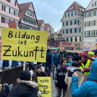 Schüler, Lehrer und Eltern halten bunte Protestplakate auf dem Tübinger Marktplatz hoch. Sie zeigen Gemeinderat und Stadtverwaltung, dass sie gegen die Sparpläne an Schulen sind.