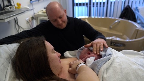 Eine Frau im Krankenbett, mit ihrem Neugeborenen auf der Brust und einem Mann kniend neben ihr - die frisch gebackenen Eltern haben zum Jahresende im Zollernalbklinikum noch einmal Zuwachs bekommen.