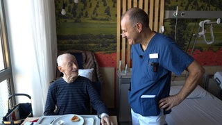 Ein Patient in einem Krankenzimmer bekommt von Arzt Volker Damm aufmunternde Worte