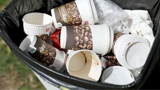 Kaffeebecher und andere Einwegverpackungen liegen in einem Mülleimer.