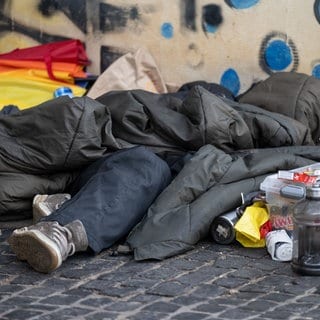 Ein Schlafsack bedeckt eine obdachlose Person. Daneben stehen Essen und Trinken. Für Obdachlose gibt es in Tübingen mehrere Unterkünfte.