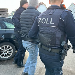 Zwei bewaffnete Zollbeamte führen einen Mann ab. Am Dienstag gab es eine Razzia in Tübingen wegen des Verdachts auf Schwarzwarbeit auf Baustellen.