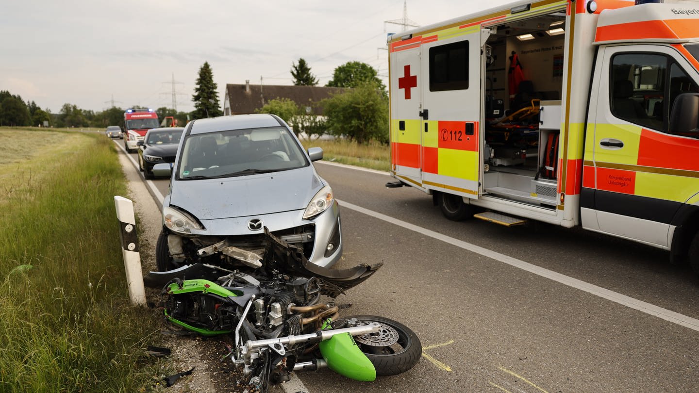 Ein beschädigtes Auto und Motorrad stehen nach einem Unfall am Straßenrand, daneben ein Rettungswagen. Bei einem Zusammenstoß mit einem Auto nahe Unterroth im Kreis Neu-Ulm ist am Donnerstagabend ein 20-jähriger Motorradfahrer getötet worden.
