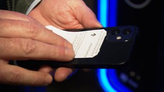 Ein Mann hält ein Parkticket an ein Smartphone. Wenn das Parkticket ans Handy kommt, zerstören dessen Magneten die Informationen auf dem braunen Magnetstreifen. Die Ausfahrt aus dem Parkhaus in Ulm ist dann nicht mehr möglich.