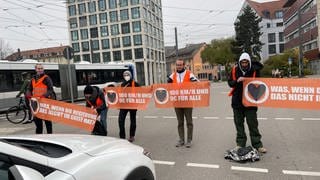 Klimaaktivisten blockieren mit Bannern Straße. In Ulm haben Aktivisten der Bewegung "Letzte Generation" sich dann auf der Fahrbahn festgeklebt. 