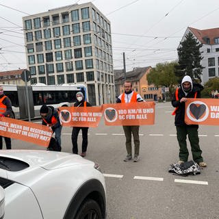 Klimaaktivisten blockieren mit Bannern Straße. In Ulm haben Aktivisten der Bewegung "Letzte Generation" sich dann auf der Fahrbahn festgeklebt. 