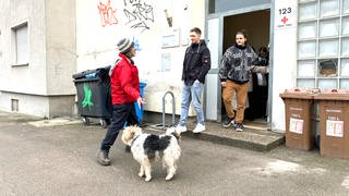 Ein Mann mit Hut und Hund vor dem Eingang zu einem Haus. Lemmy zeigt bei seiner Stadtführung den Studierenden auch das DRK-Übernachtungsheim für Wohnungslose in Ulm.