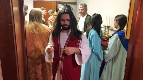 Mann mit langem schwarzen Haaren und Bart in rotem Gewand. Der "syrische Jesus" ist für den Auftritt in ein traditionelles orientalisches Gewand gekleidet.