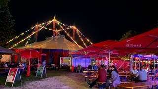 Ein bunt beleuchtes Zirkuszelt, davor Bierbänke mit Publikum. Das Ulmer Zelt im Jahr hat das Programm für die Saison 2023 vorgestellt (Archivbild).