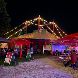 Ein bunt beleuchtes Zirkuszelt, davor Bierbänke mit Publikum. Das Ulmer Zelt im Jahr hat das Programm für die Saison 2023 vorgestellt (Archivbild).