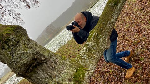 Ein Mann mit einer Kamera an einem alten Baum. Tierfotograf Jochen Bayer liebt die 400 Jahre alte Linde in seiner Heimatgemeinde Bernstadt.