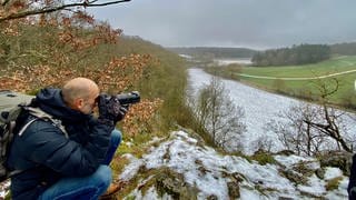Ein Mann blickt mit einer Kamera in der Hand übers Lonetal. Tierfotograf Jochen Bayer auf dem Hubertusfelsen, wo Wanderfalken brüten. 