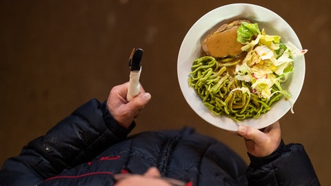 Ein Mann geht mit einem Teller Essen durch die Kirche (Symbolbild)