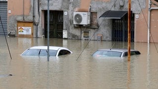 Autos stehen auf einer überschwemmten Straße im Wasser. In der italienischen Region Emilia-Romagna ist es nach heftigen Regenfällen zu teils dramatischen Überschwemmungen gekommen