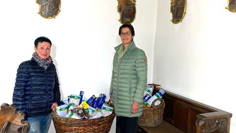  Zwei Frauen mit Körben voller Lebensmittel in einer Kirche. Rosl Baur und Susanne Backes-Keck kümmern sich ehrenamtlich um die Körbe mit Lebensmitteln, die in katholischen Kirchen in Niederstotzingen für Bedürftige bereitstehen.