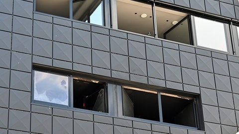 Die in Quadrate aufgeteilte anthrazitfarbene Fassade des Magietheaters in Neu-Ulm. Oben sind geöffnete Fenster zu sehen, darunter ebenfalls. Dort sind die Fenster von der Hitze zerstört worden. An der Fassade selbst sind keine Schäden zu sehen. 