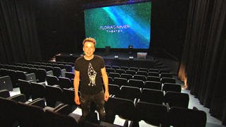 Florian Zimmer steht im Showroom seines Theaters zwischen den leeren Zuschauersesseln. Im Hintergrund ist sein Name auf einem großen Bildschirm zu sehen. Zimmer hofft, nach dem Brand schnell wieder öffnen zu können.