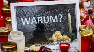 Am Tatort in Illerkirchberg haben Passanten Kerzen, Blumen und einen Bilderrahmen mit dem Wort "Warum?" abgelegt. (Archivbild)
