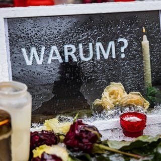 Am Tatort in Illerkirchberg haben Passanten Kerzen, Blumen und einen Bilderrahmen mit dem Wort "Warum?" abgelegt. (Archivbild)